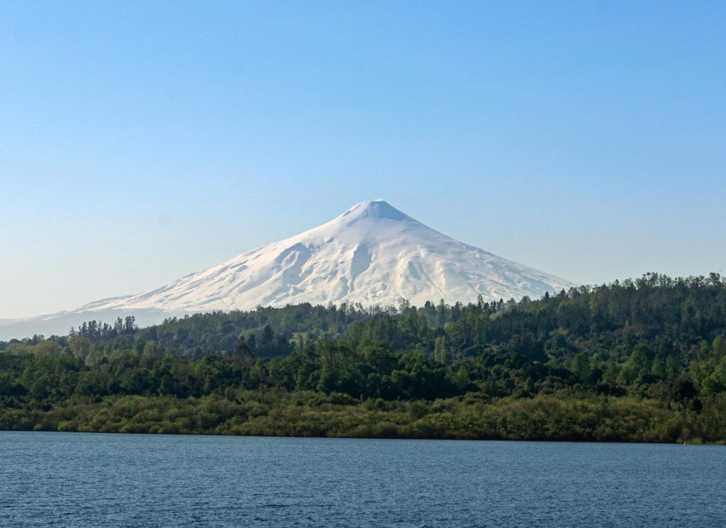 A stunning capture of Villarrica Volcano with snow-covered peak and calm lake, Chile.