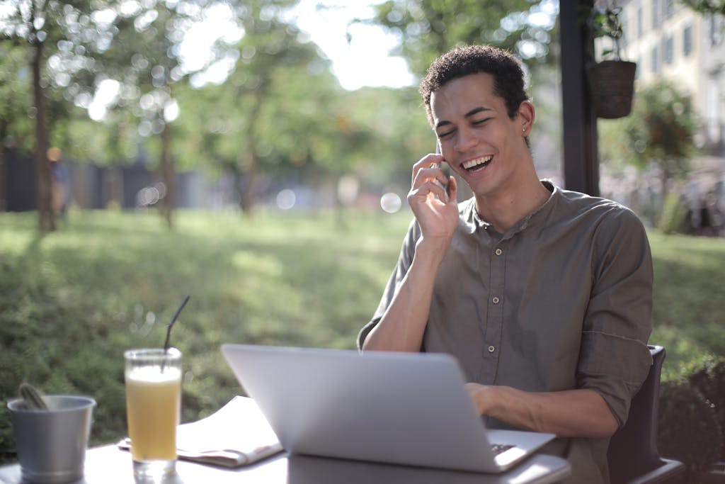 Content African American male freelancer wearing casual clothes sitting at table in street cafe possibly in Chile with laptop and speaking on cellphone to illustrate making calls with a Chilean SIM card while working on startup