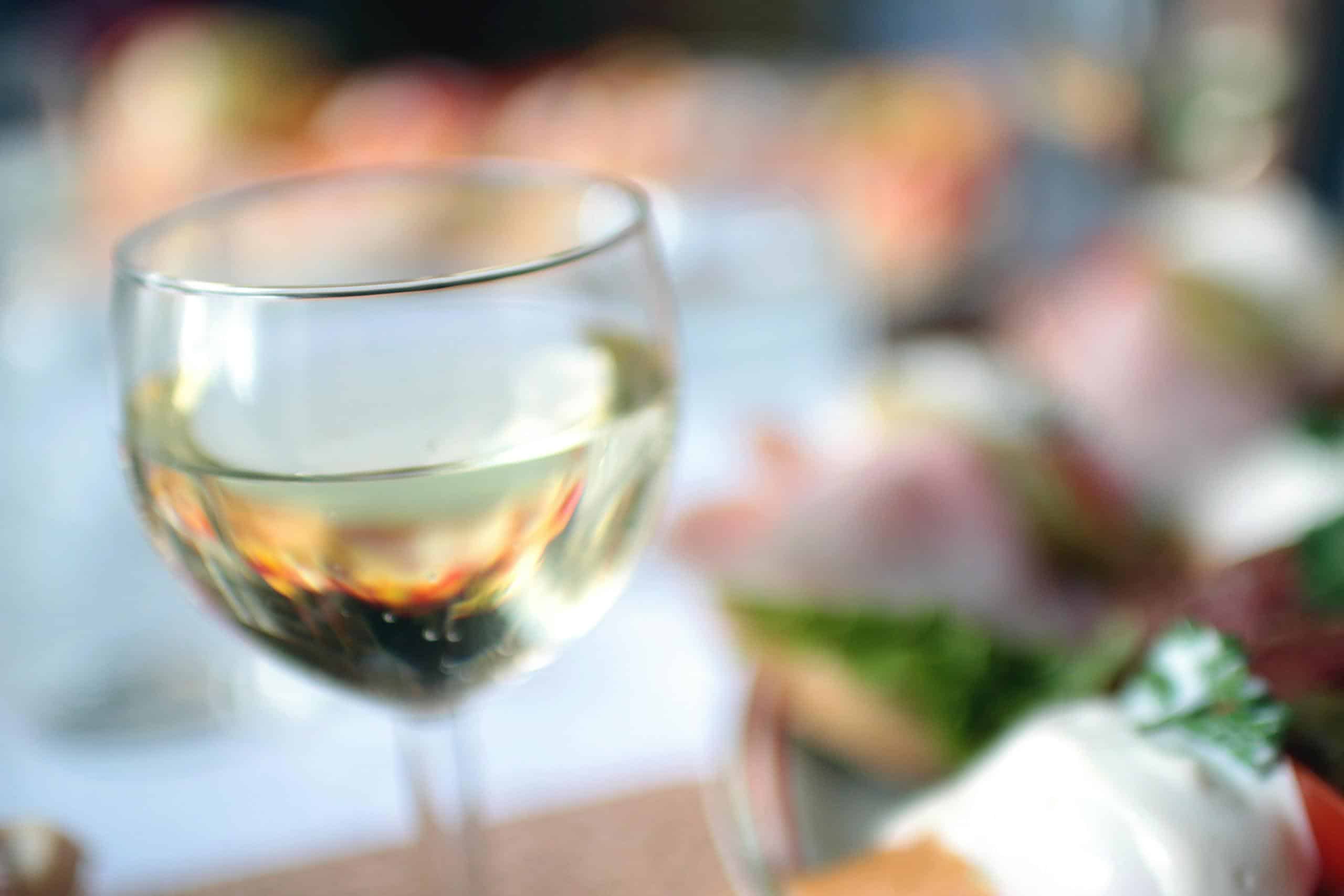 A close-up of a white wine glass in a blurred lunch ambiance.