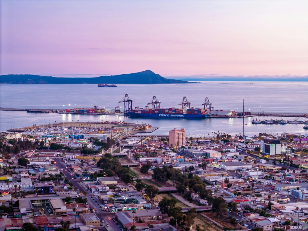 A stunning view of a coastal port city at twilight with a container ship docked.
