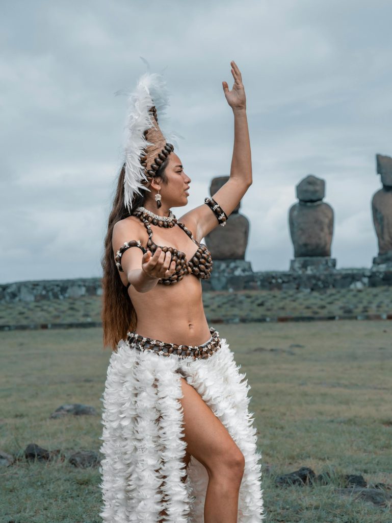 A woman dances in traditional attire near iconic Moai statues on Easter Island, Chile.