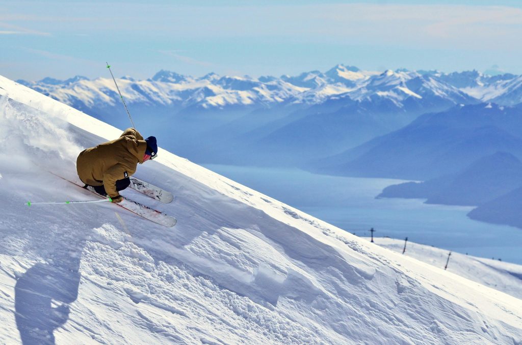 Experience an exhilarating skiing descent on pristine snowy slopes with majestic mountains in the background.