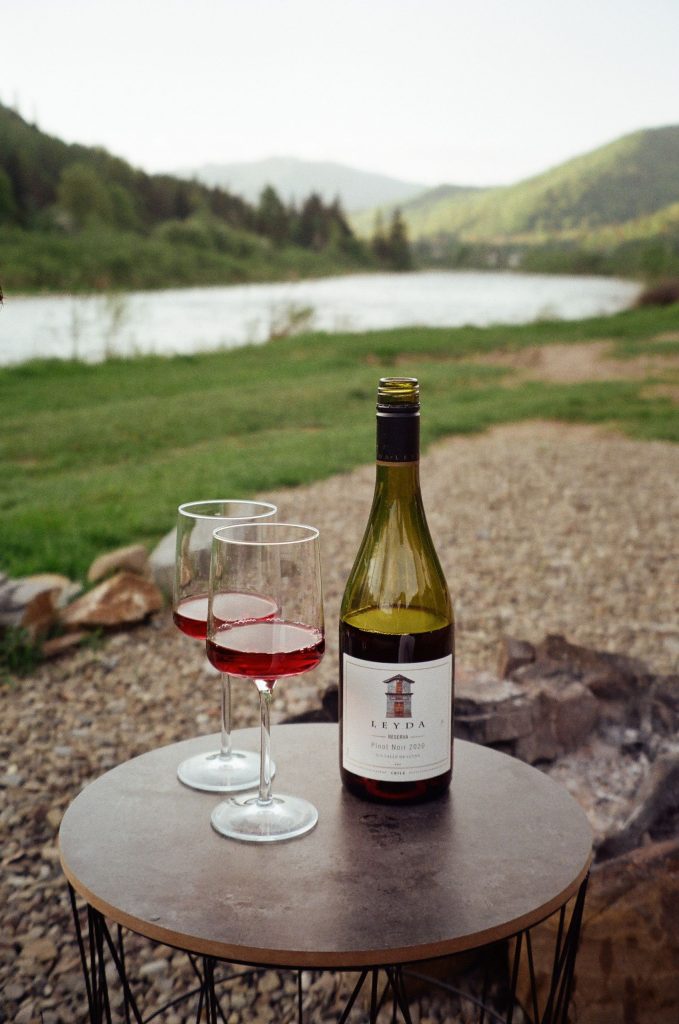Enjoy a serene outdoor setting with a bottle of Pinot Noir and wineglasses on a table.
